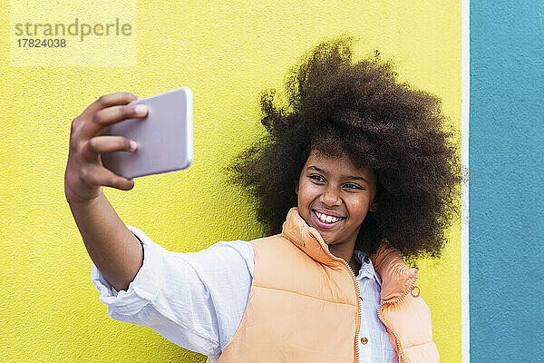 Glückliches Mädchen  das ein Selfie mit dem Smartphone vor einer gelben und blauen Wand macht