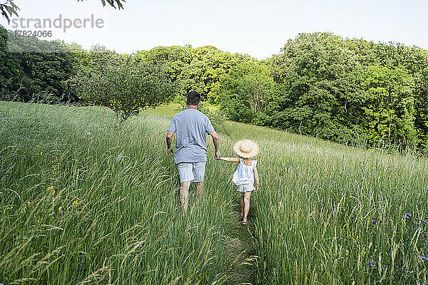 Vater und Tochter gehen Händchen haltend durch das Feld