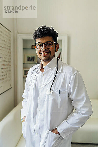 Lächelnder junger Arzt mit der Hand in den Taschen im Krankenhaus