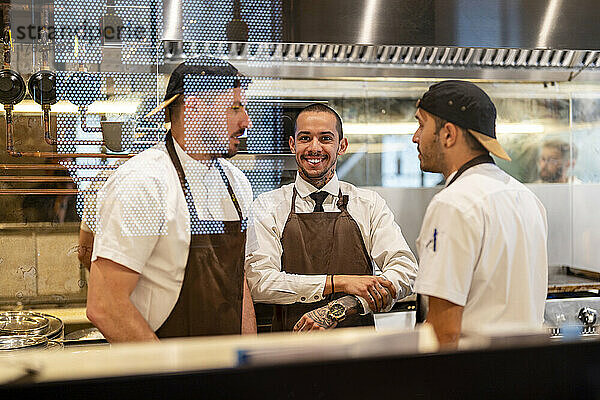 Lächelnder Koch steht mit Kollegen im Blick durch Glas