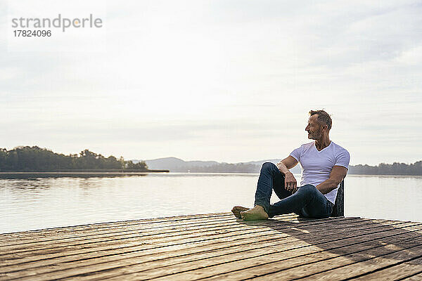 Reifer Mann sitzt auf Steg am See