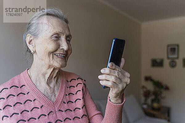 Lächelnde Frau  die zu Hause per Videoanruf über ihr Smartphone spricht