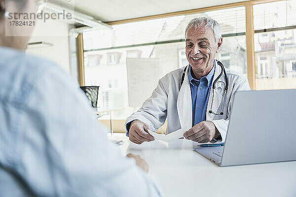 Glücklicher Arzt  der mit dem Patienten in der Klinik über das Dokument spricht
