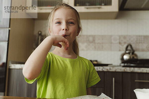 Lächelndes Mädchen leckt zu Hause in der Küche den Finger