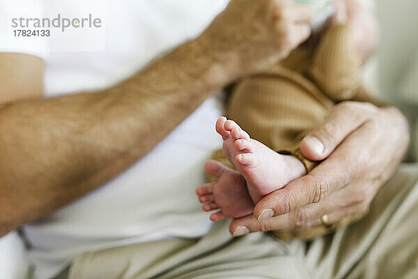 Hand eines Mannes  der sein Baby zu Hause trägt