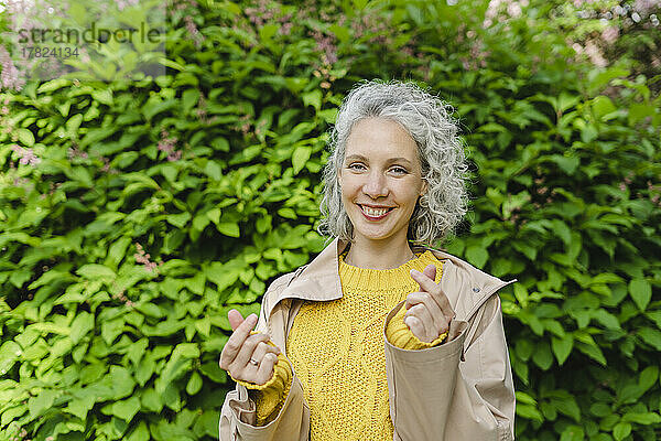Glückliche Frau formt mit den Fingern im Park ein Herz