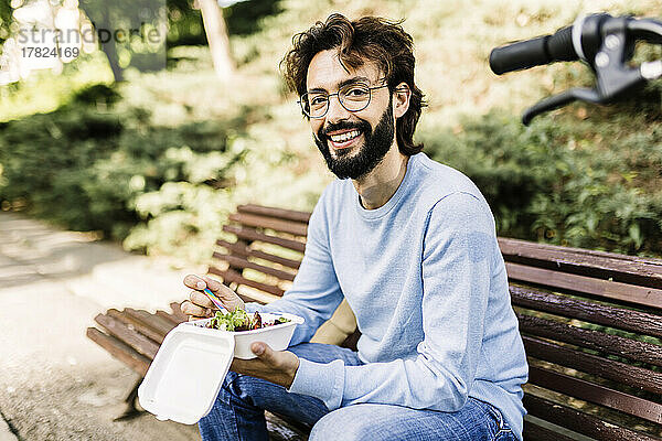 Glücklicher Mann mit Essen sitzt auf einer Bank im Park