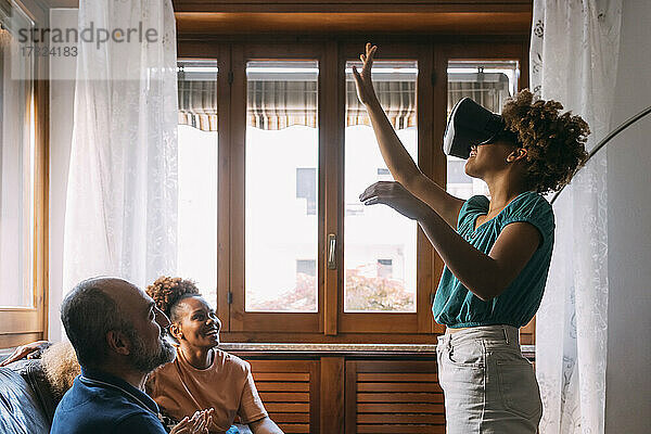 Mädchen mit Virtual-Reality-Simulator gestikuliert vor der Familie zu Hause