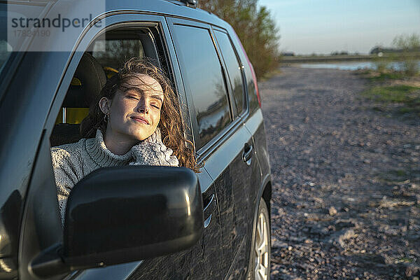 Lächelnde Frau mit geschlossenen Augen sitzt im Auto
