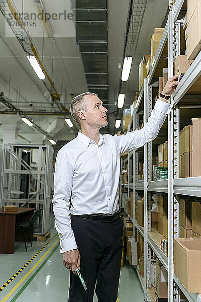 Geschäftsmann untersucht Maschinenteil auf Regal in Fabrik