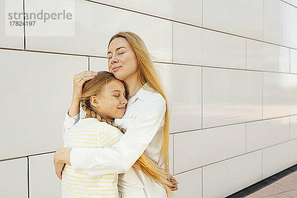 Glückliche Mutter umarmt Tochter vor der Wand