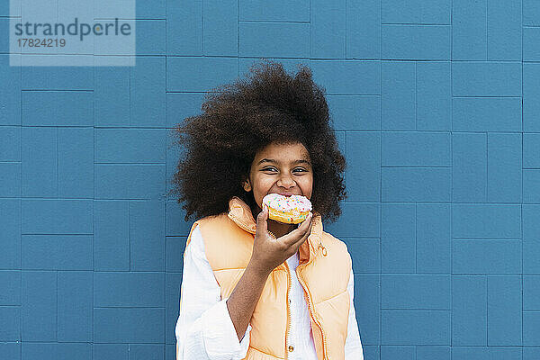 Mädchen isst Donut und steht vor blauer Wand