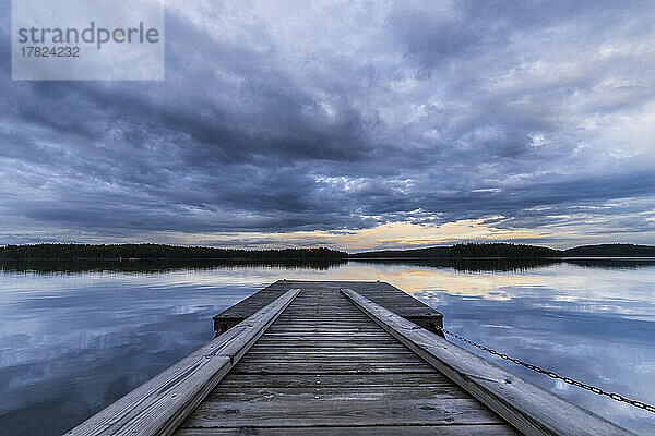 Schweden  Kreis Vastra Gotaland  Bewölkter Himmel über dem Steg am Ufer des Sees Vastra Silen in der Abenddämmerung