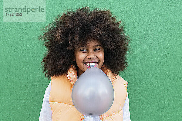 Happy girl holding balloon in mouth against green background