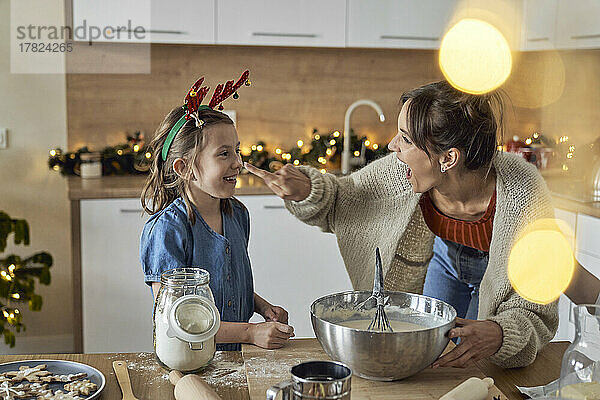 Glückliche Mutter streut ihrer Tochter in der Küche Mehl auf die Nase