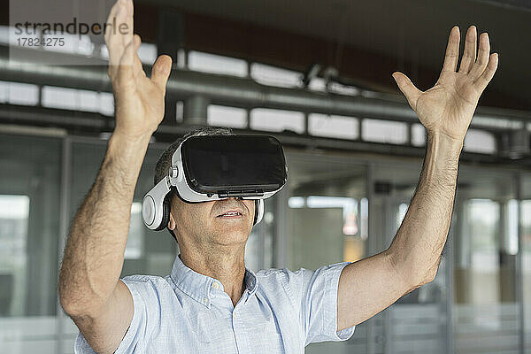 Reifer Geschäftsmann mit Virtual-Reality-Simulator gestikuliert im Büro