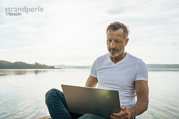 Reifer Freiberufler nutzt Laptop am Seeufer