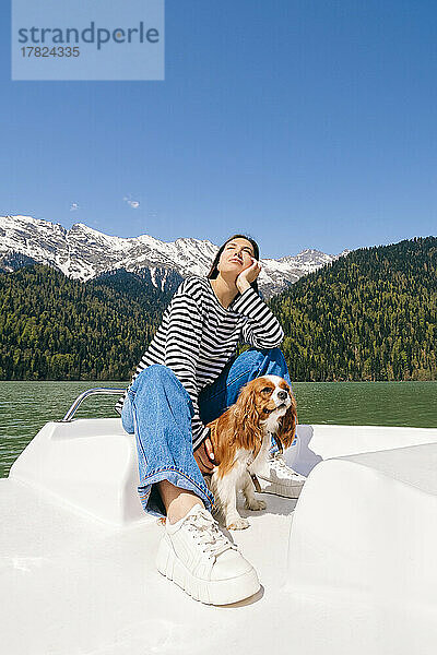 Frau mit Hund genießt sonnigen Tag auf dem Boot am Ritsa-See