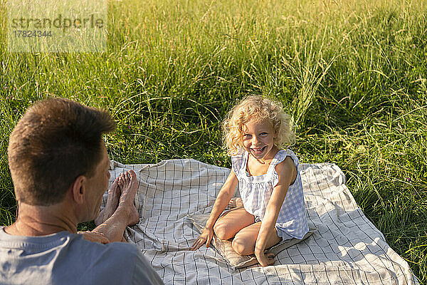 Fröhliches blondes Mädchen sitzt mit Vater auf einer Picknickdecke