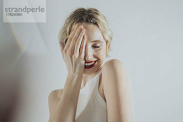 Schüchterne Frau bedeckt Augen mit der Hand vor weißem Hintergrund