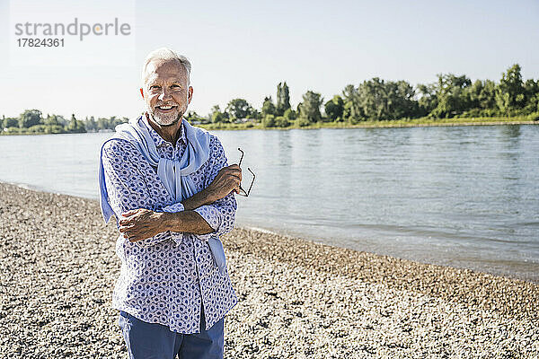 Lächelnder Mann mit verschränkten Armen und Brille am Flussufer