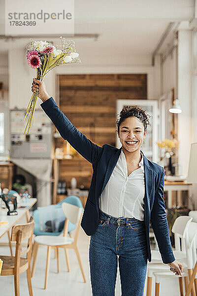 Fröhliche junge Geschäftsfrau steht mit Blumen im Büro