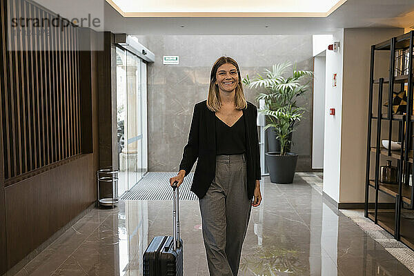Glückliche Geschäftsfrau mit Koffer  die das Hotel betritt