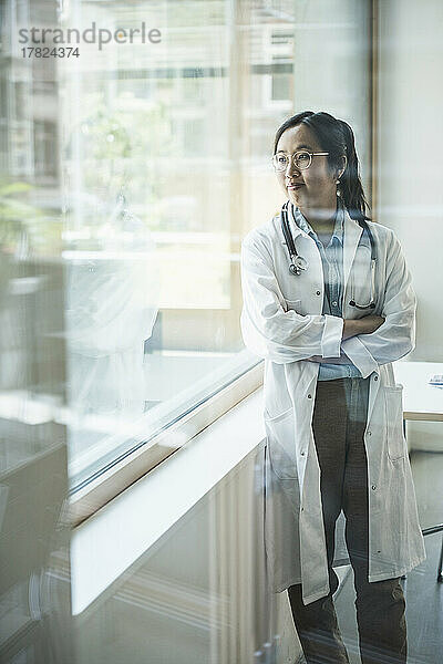 Smiling doctor with arms crossed looking through window