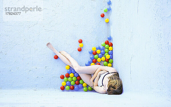 Woman with multi colored plastic balls sitting by blue pool wall