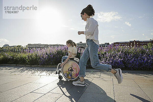 Mutter rennt Tochter im Rollstuhl im Park hinterher