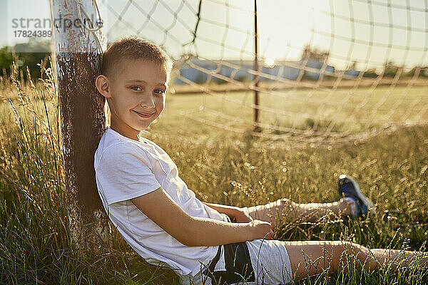 Lächelnder Junge  der auf einer Stange sitzt und auf dem Sportplatz sitzt