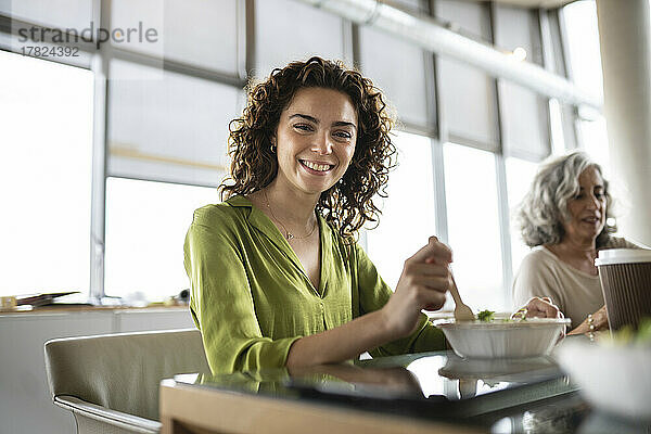 Lächelnde Geschäftsfrau mit einer Schüssel Salat am Schreibtisch