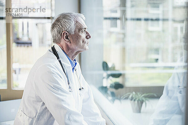 Arzt blickt durch Fenster im Krankenhaus