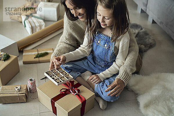 Lächelndes Mädchen und Mutter mit Dekorationsschachtel  die zu Hause Geschenke verpackt