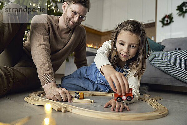 Lächelnder Mann und Tochter spielen zu Hause mit Miniaturzug