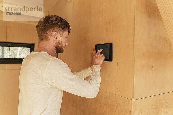 Der Mann richtet mit einem Tablet an der Wand eines Öko-Hauses eine Smart-Home-Einheit ein