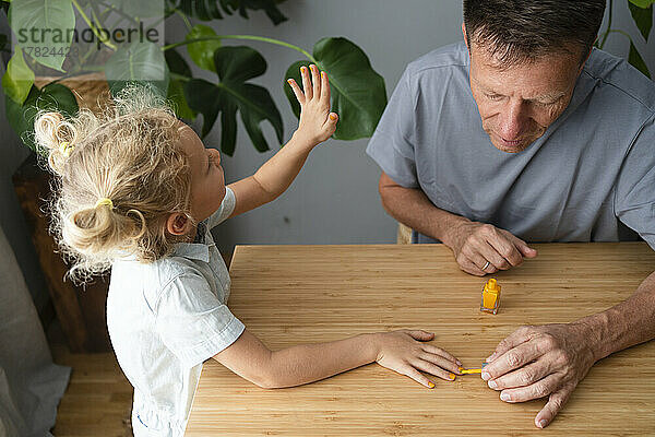 Vater trägt zu Hause Nagellack auf die Nägel seiner Tochter auf