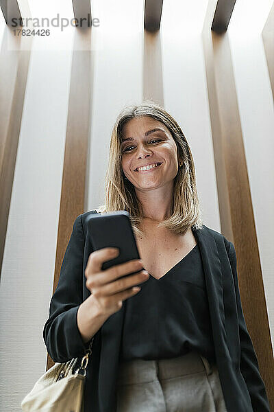 Glückliche Geschäftsfrau benutzt Smartphone vor der Wand