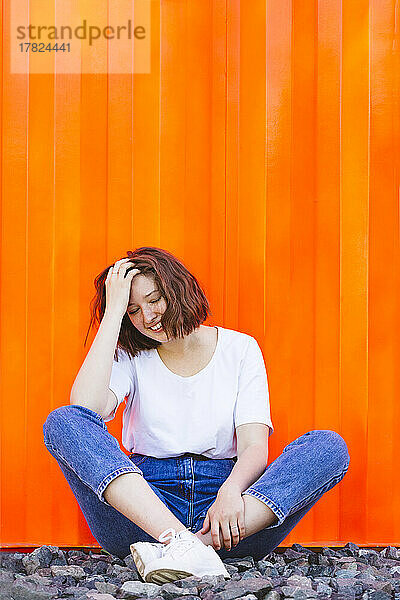 Smiling teenage girl with eyes closed sitting in front of orange cargo container