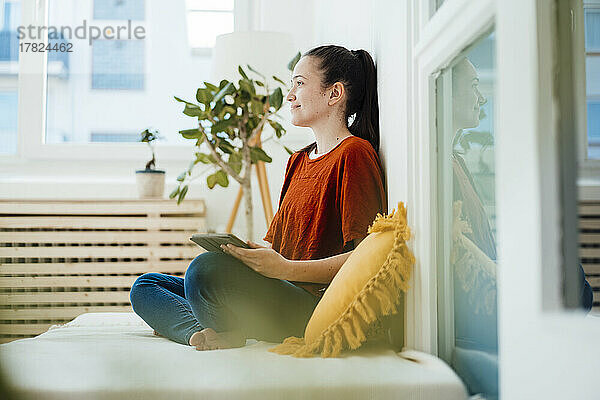 Nachdenkliche Frau mit Tablet-PC im Wohnzimmer