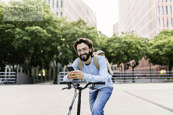 Glücklicher Mann mit Fahrrad und Handy im Park