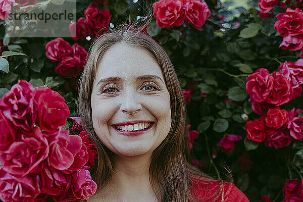 Glückliche Frau inmitten eines Busches aus roten Rosen