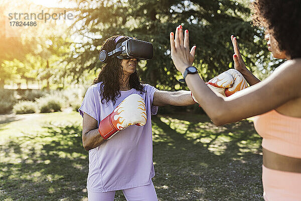 Ältere Frau mit VR-Brille boxt mit Tochter im Park