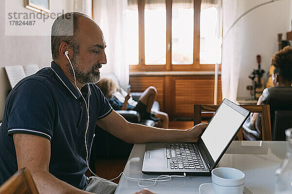 Geschäftsmann trägt In-Ear-Kopfhörer und führt zu Hause Videoanrufe über den Laptop