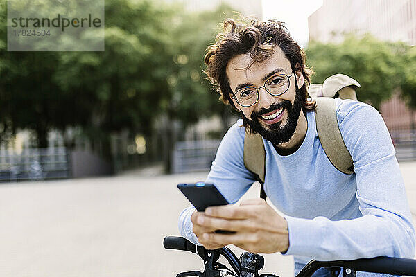 Lächelnder Mann mit Fahrrad und Mobiltelefon