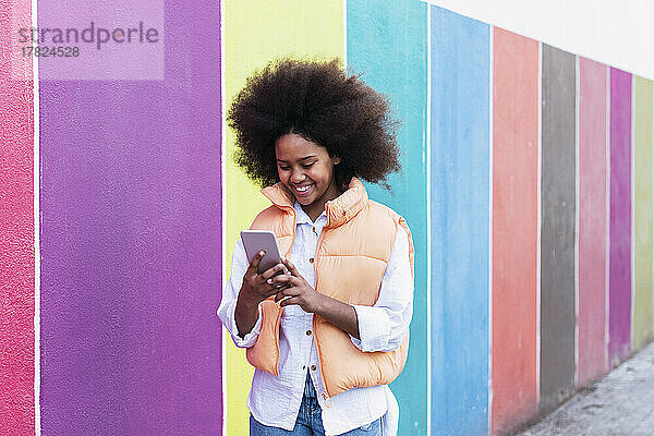 Lächelndes Mädchen  das mit seinem Smartphone an einer bunten Wand im Internet surft