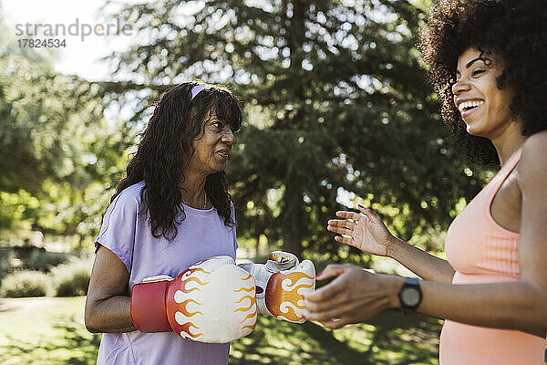 Frau lacht mit Mutter mit Boxhandschuhen im Park