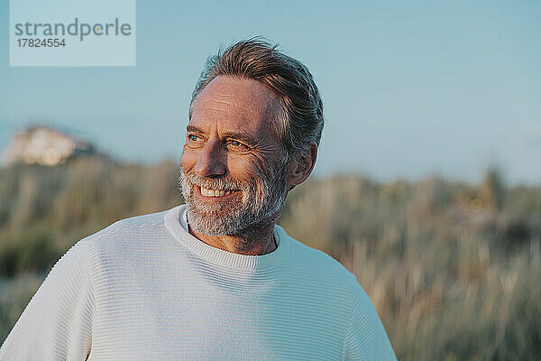 Happy mature man with beard looking away at beach