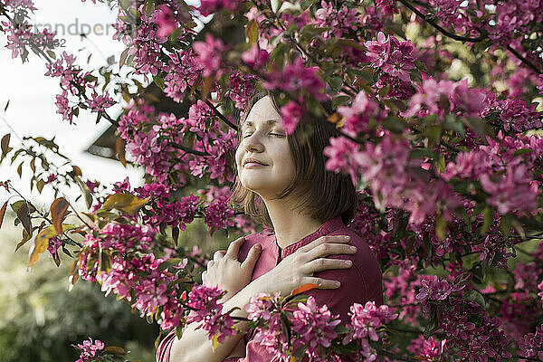Lächelnde Frau mit geschlossenen Augen  die inmitten rosa Blumen steht