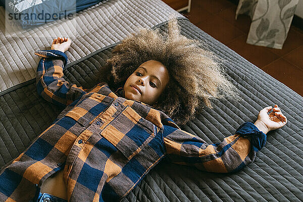 Boy with Afro hairstyle lying on bed at home